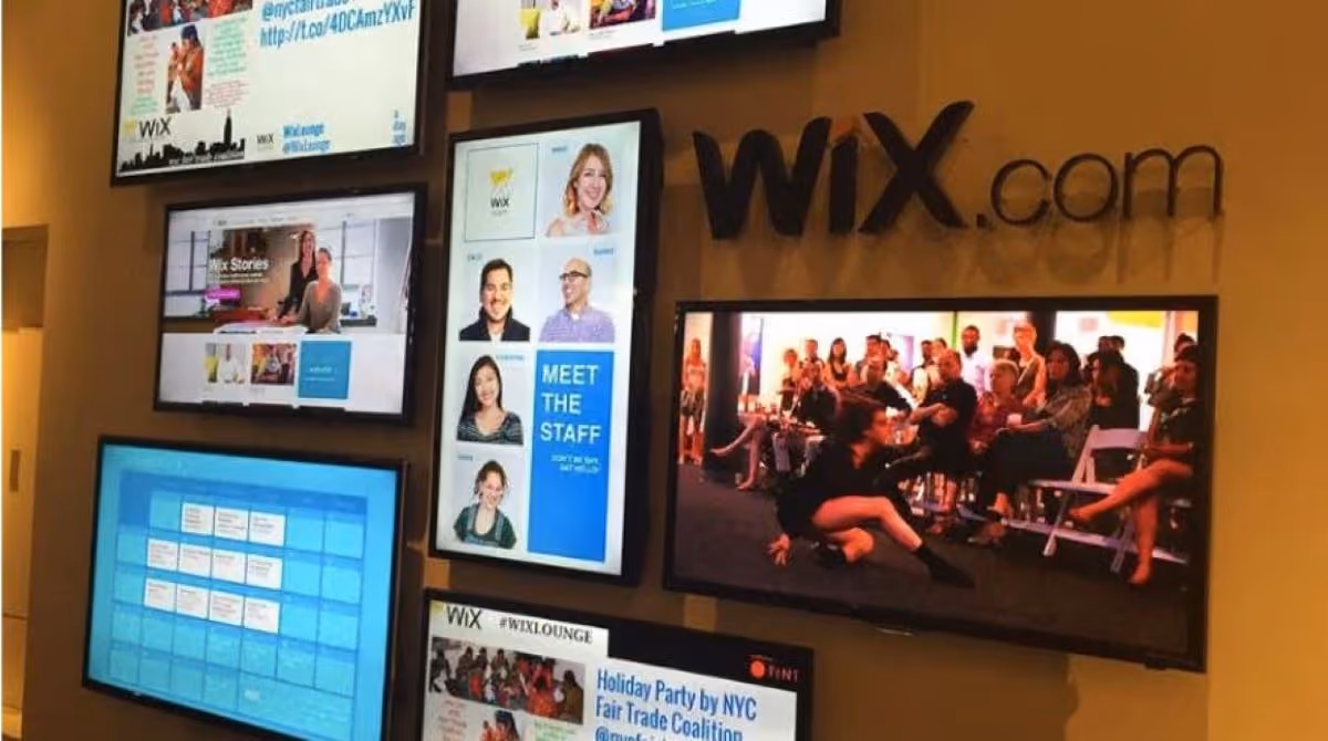 Image of several screens that appear to be mounted on the side of a wall. Most of the screens are displaying social media feeds,. There is also one screen in the bottom left corner that appears to be displaying a calendar.