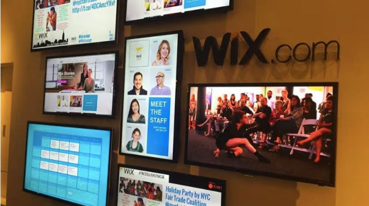 Image of several screens that appear to be mounted on the side of a wall. Most of the screens are displaying social media feeds,. There is also one screen in the bottom left corner that appears to be displaying a calendar. 