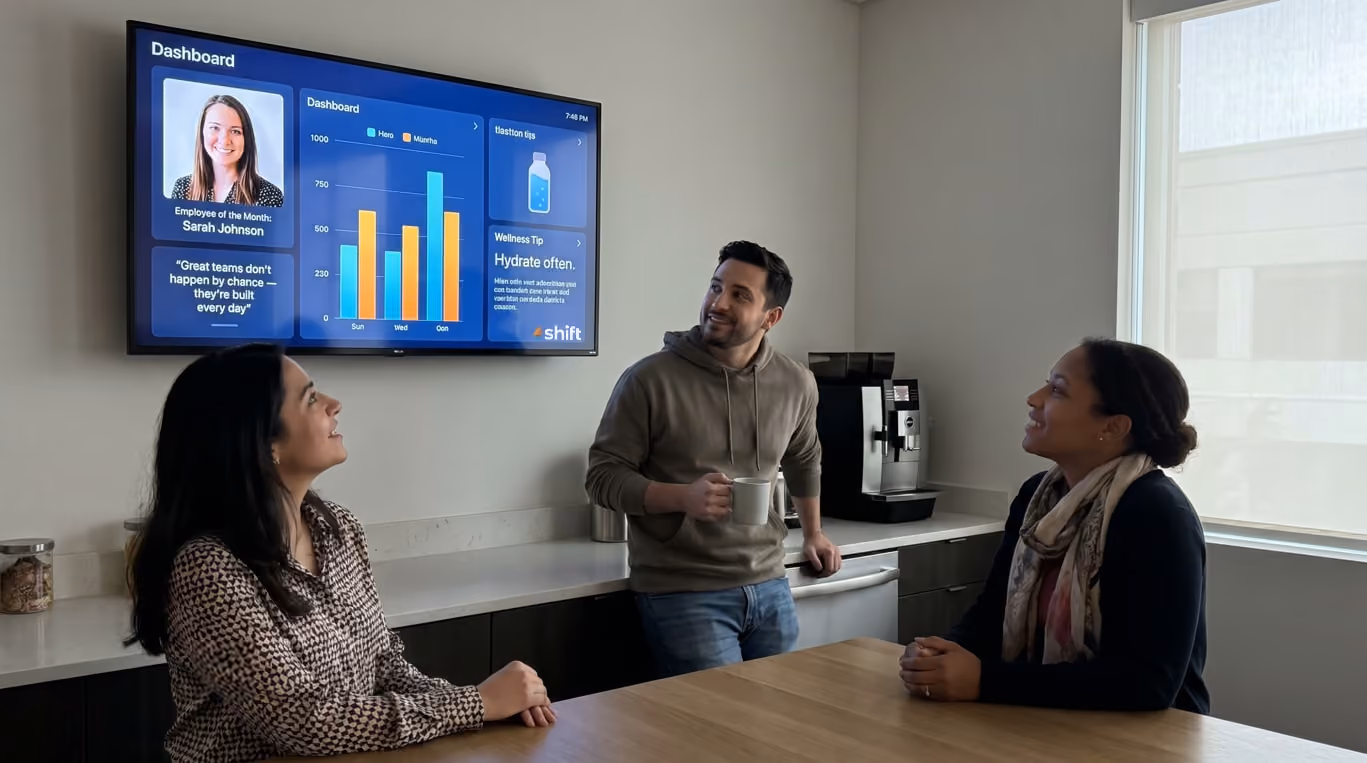Office meeting with employees discussing events listed on a wall screen, including an all-hands meeting and volunteer day.