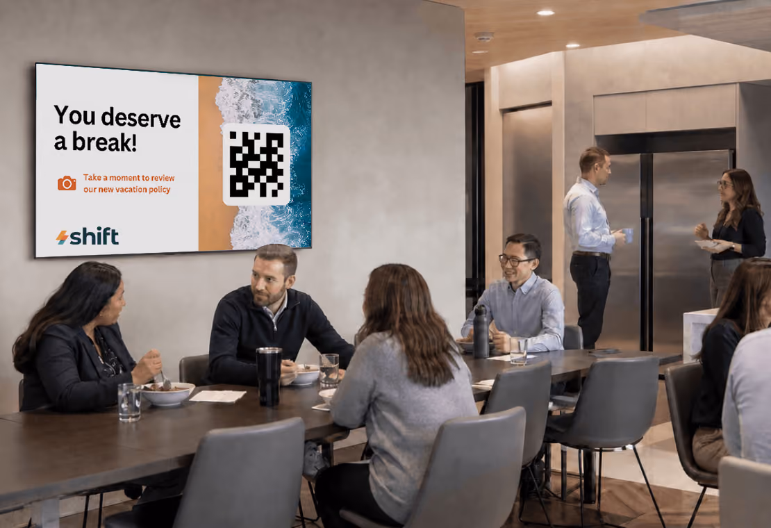 Office meeting with employees discussing events listed on a wall screen, including an all-hands meeting and volunteer day.