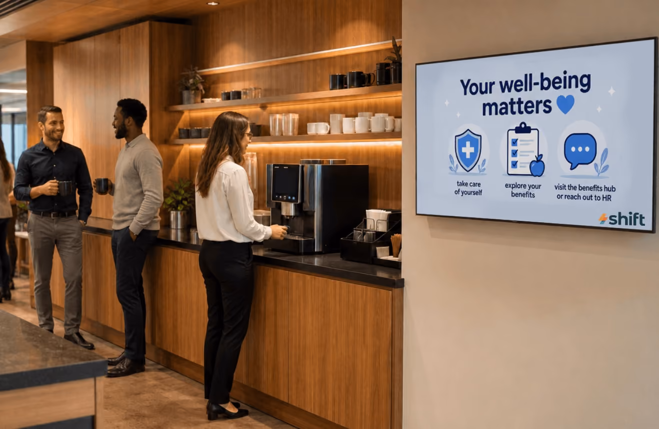 A group of people stands in front of a TV displaying the text "Your Well Being Master," engaged in discussion.