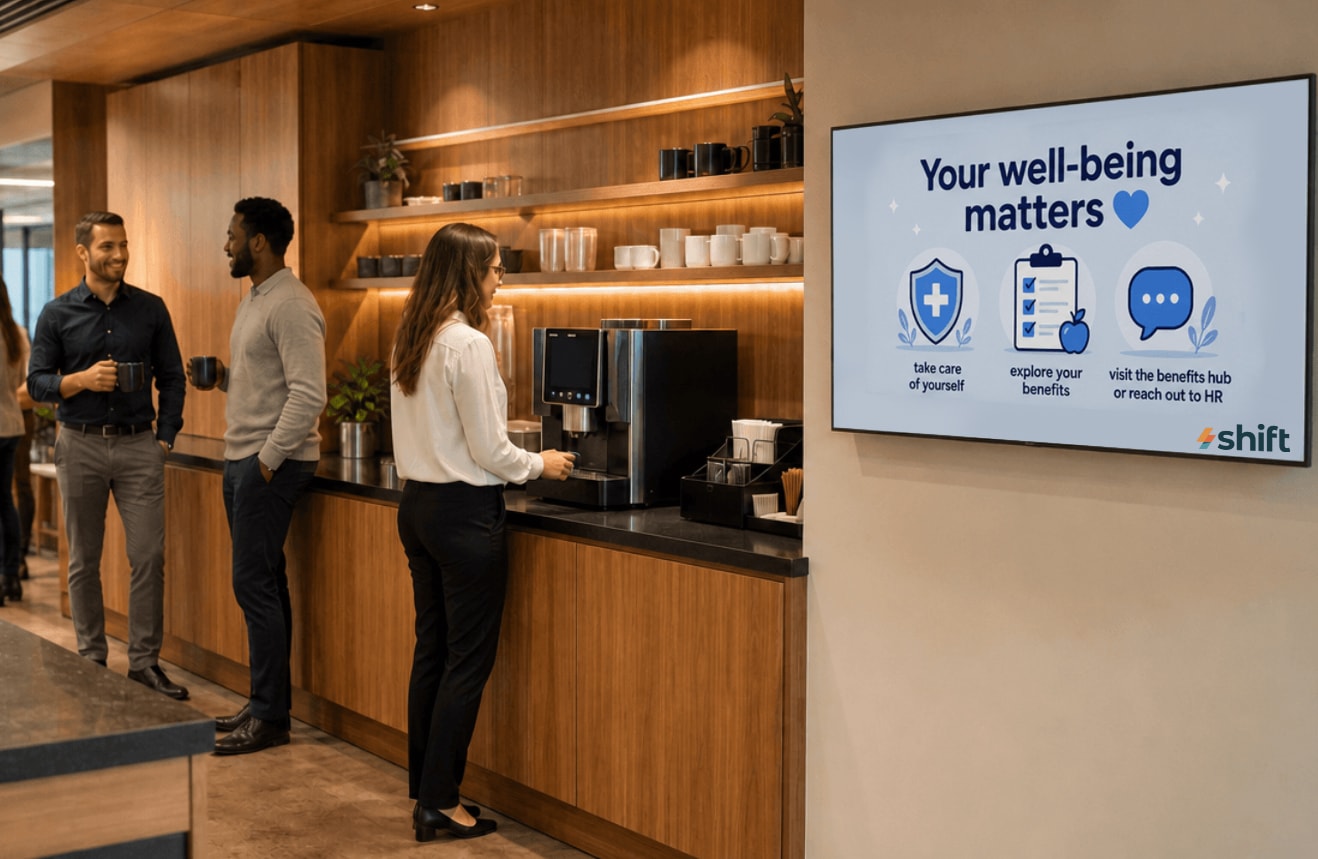 A group of people stands in front of a TV displaying the text "Your Well Being Master," engaged in discussion.