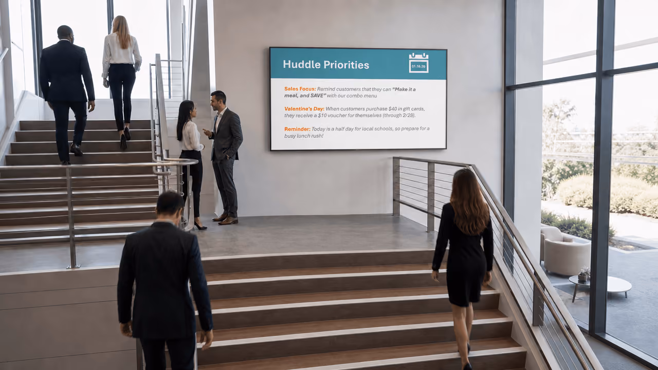People walking in an office setting up a flight of stairs with a digital screen on the wall
