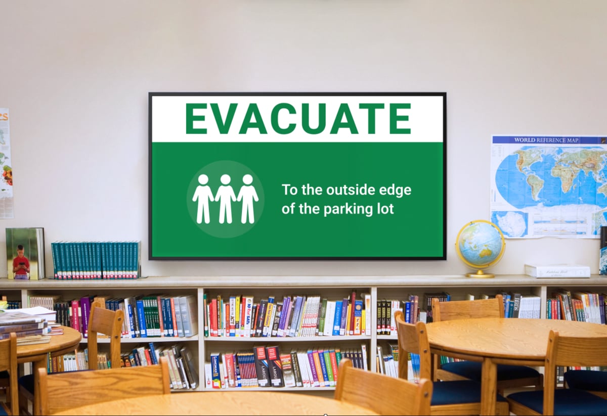 Classroom interior featuring a sign instructing to evacuate to the outside edge of the parking lot.