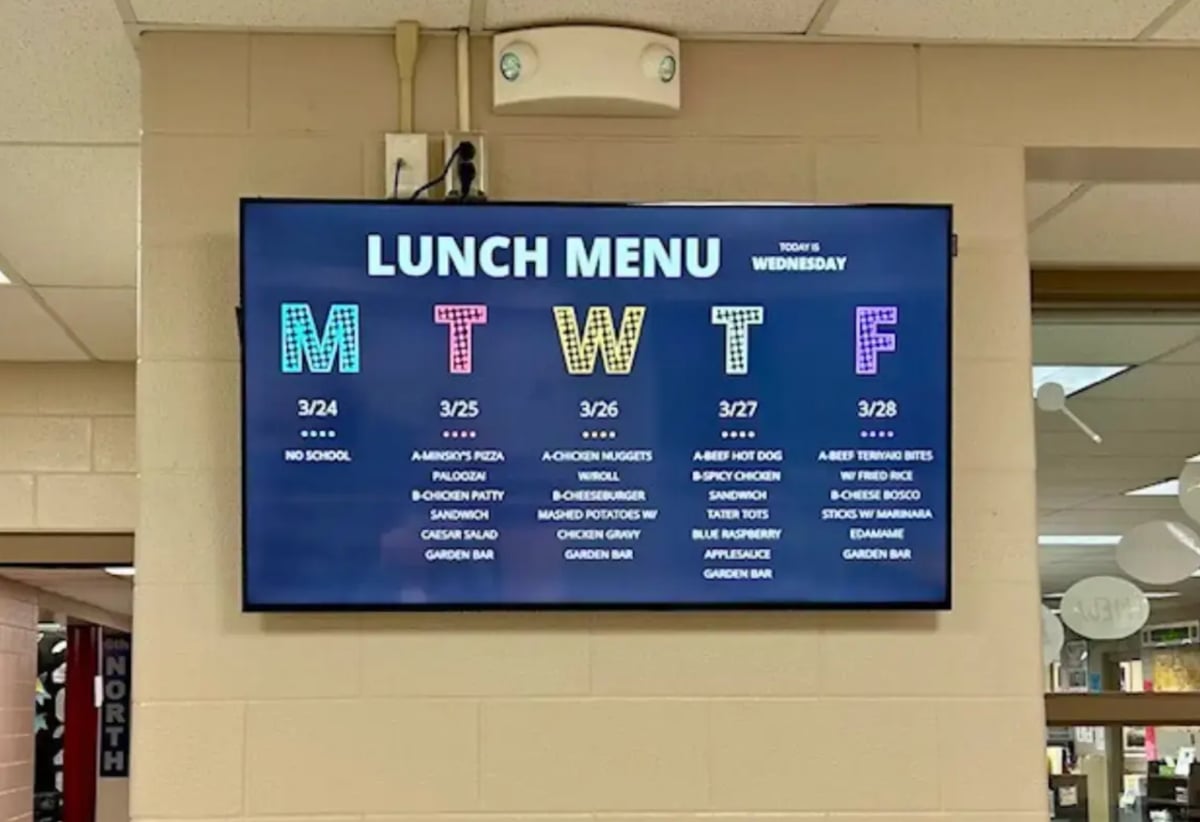A large screen shows the school lunch menu, featuring various meal options and daily specials for students.