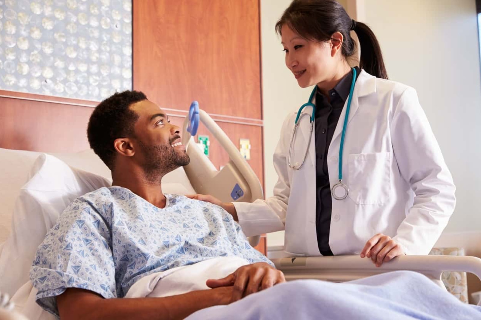 A doctor converses with a patient lying in a hospital bed, discussing treatment options and providing care.