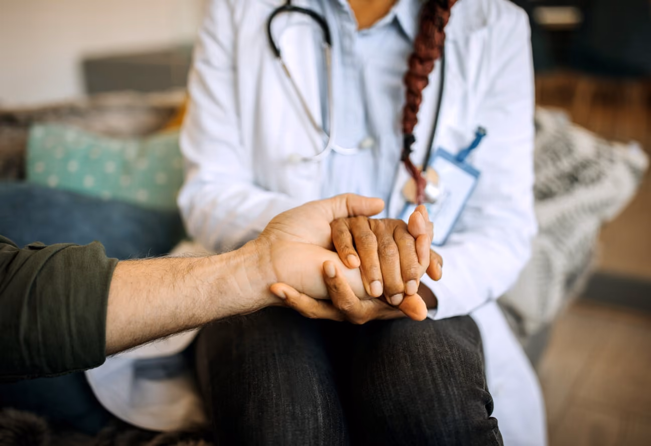 A doctor gently holds a patient's hand, conveying support and compassion during a medical consultation.
