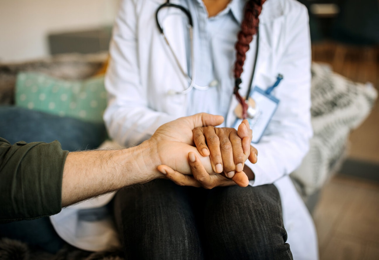 A doctor gently holds a patient's hand, conveying support and compassion during a medical consultation.