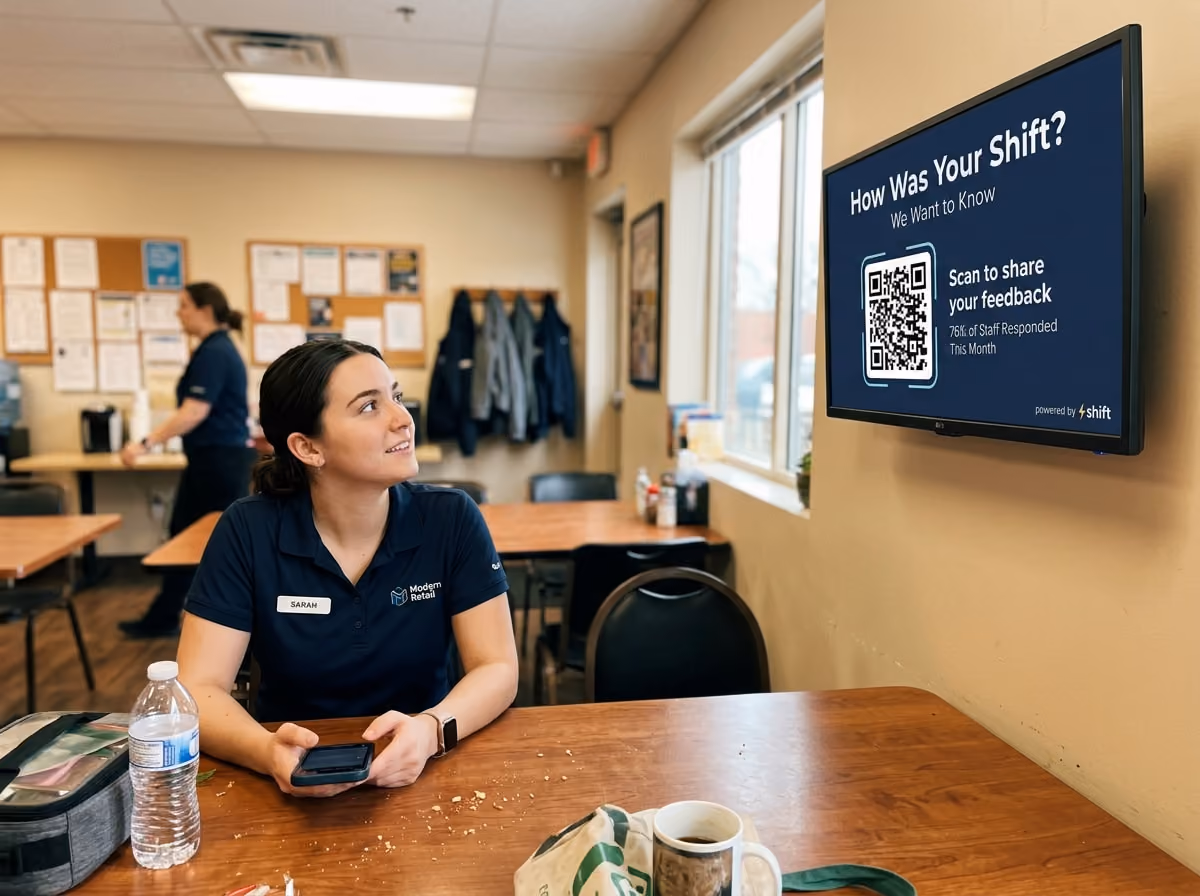 Employee in break room looks at feedback screen with QR code, phone in hand.