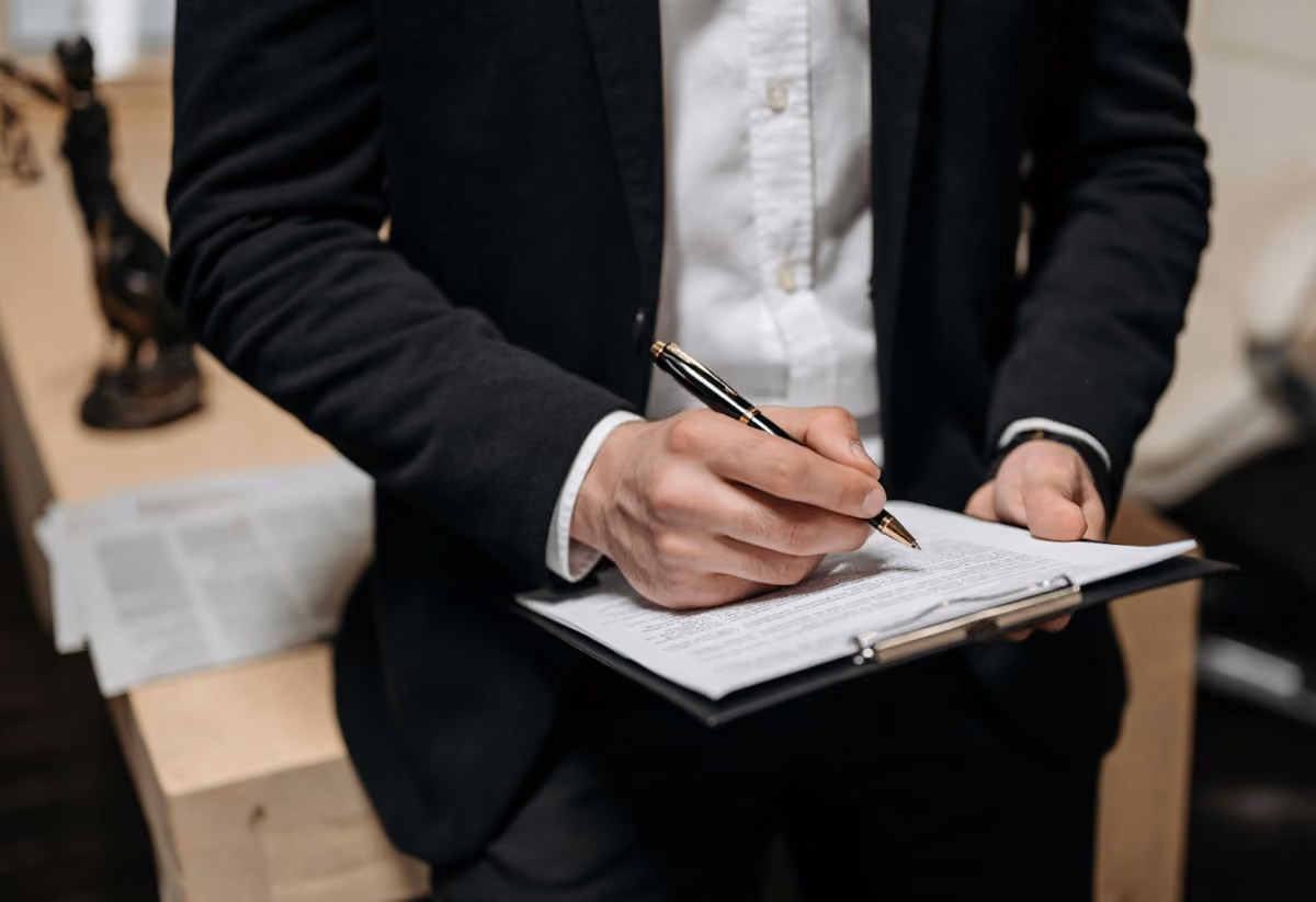 A man in a suit is focused on writing notes on a clipboard in a professional setting.