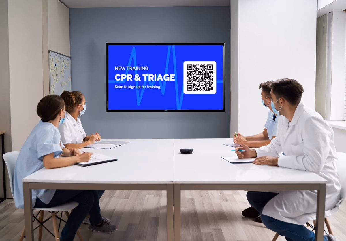 Four healthcare workers in scrubs chat in a break room, with a wellness poster on the wall promoting CPR & Triage