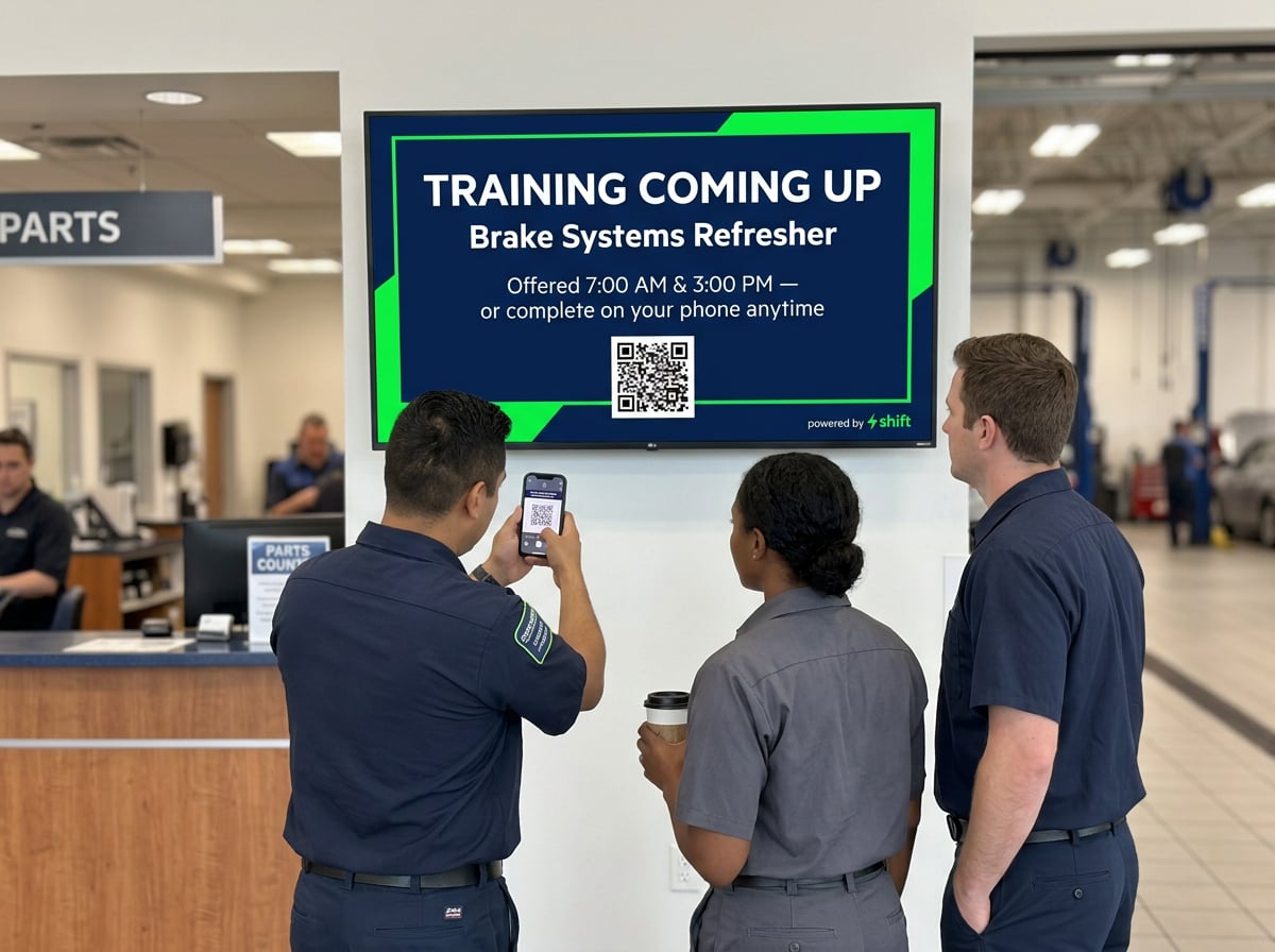 Three mechanics view a screen announcing a Brake Systems Refresher training, with one scanning a QR code using a smartphone.