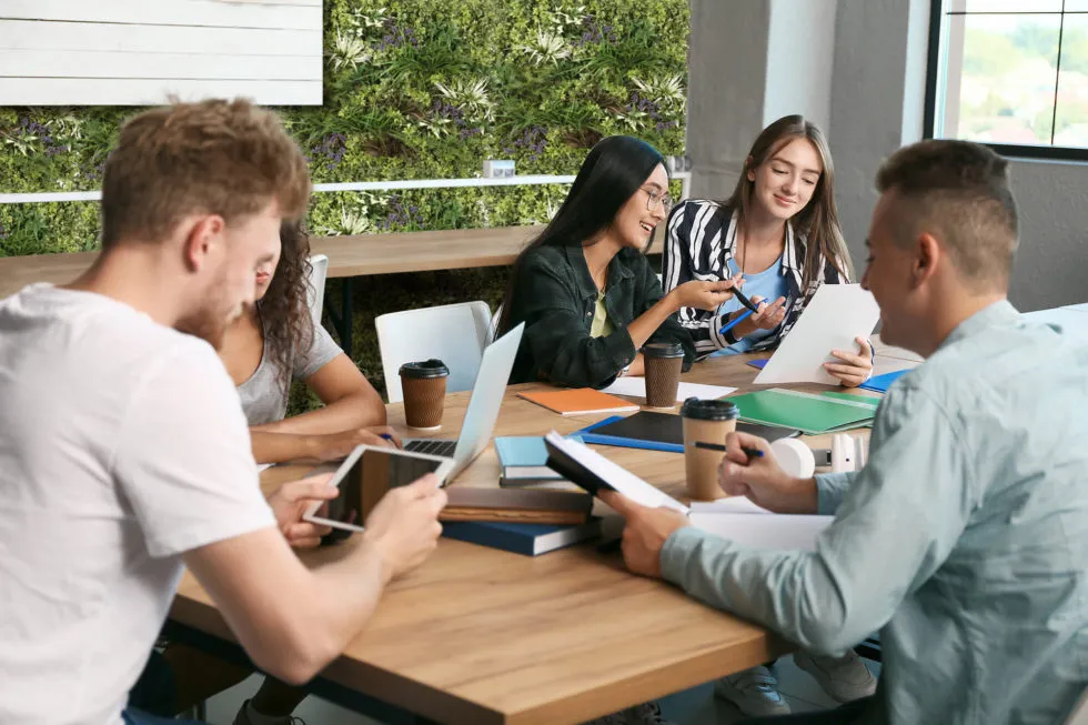 Students studying at a desk with a rear wall covered in artificial plant walls.