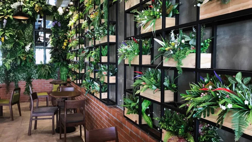Interior of a cafe with walls and shelving with artificial plant walls.