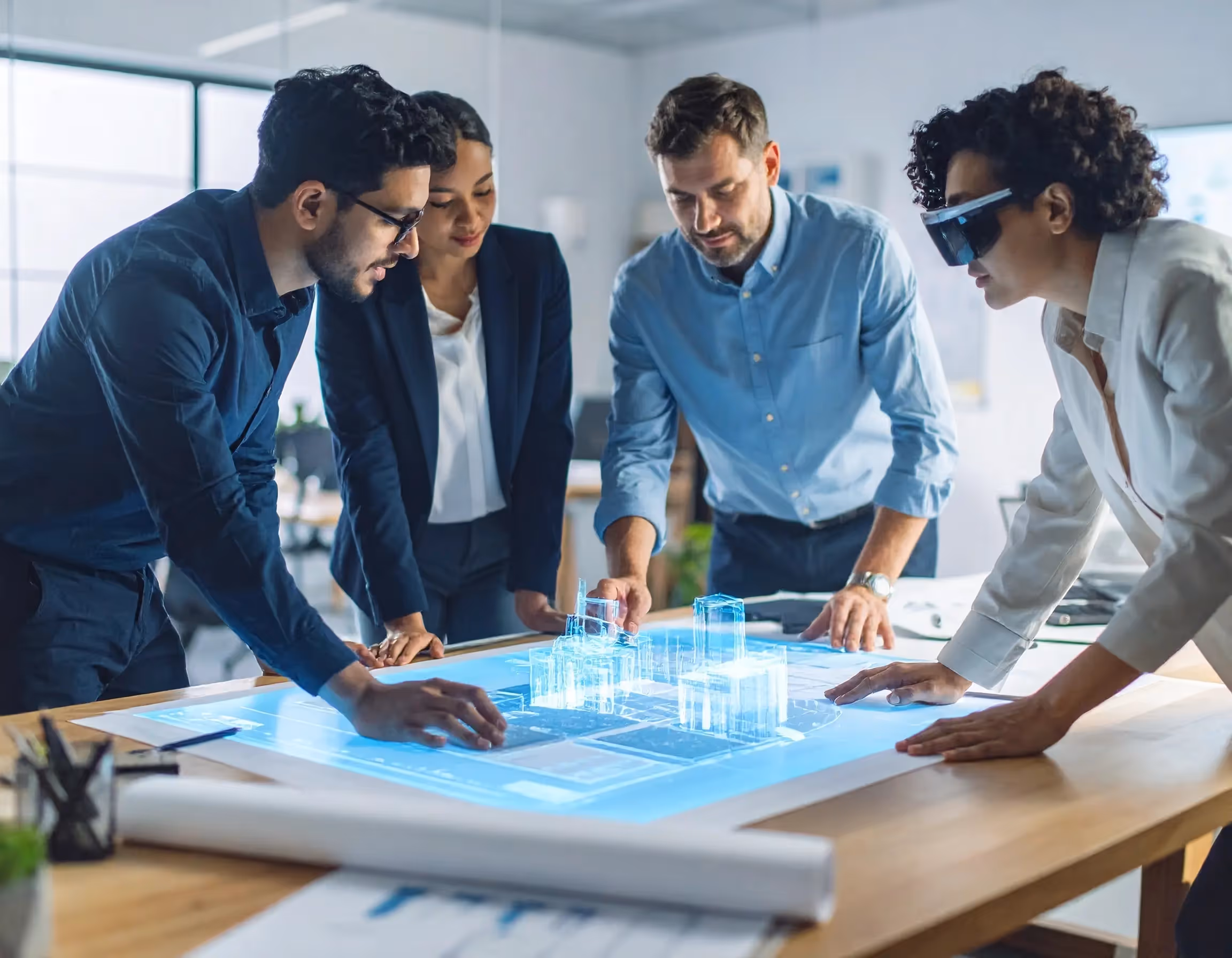 Four professionals interacting with a table projecting a 3D digital model of a cityscape, with one person wearing augmented reality glasses.