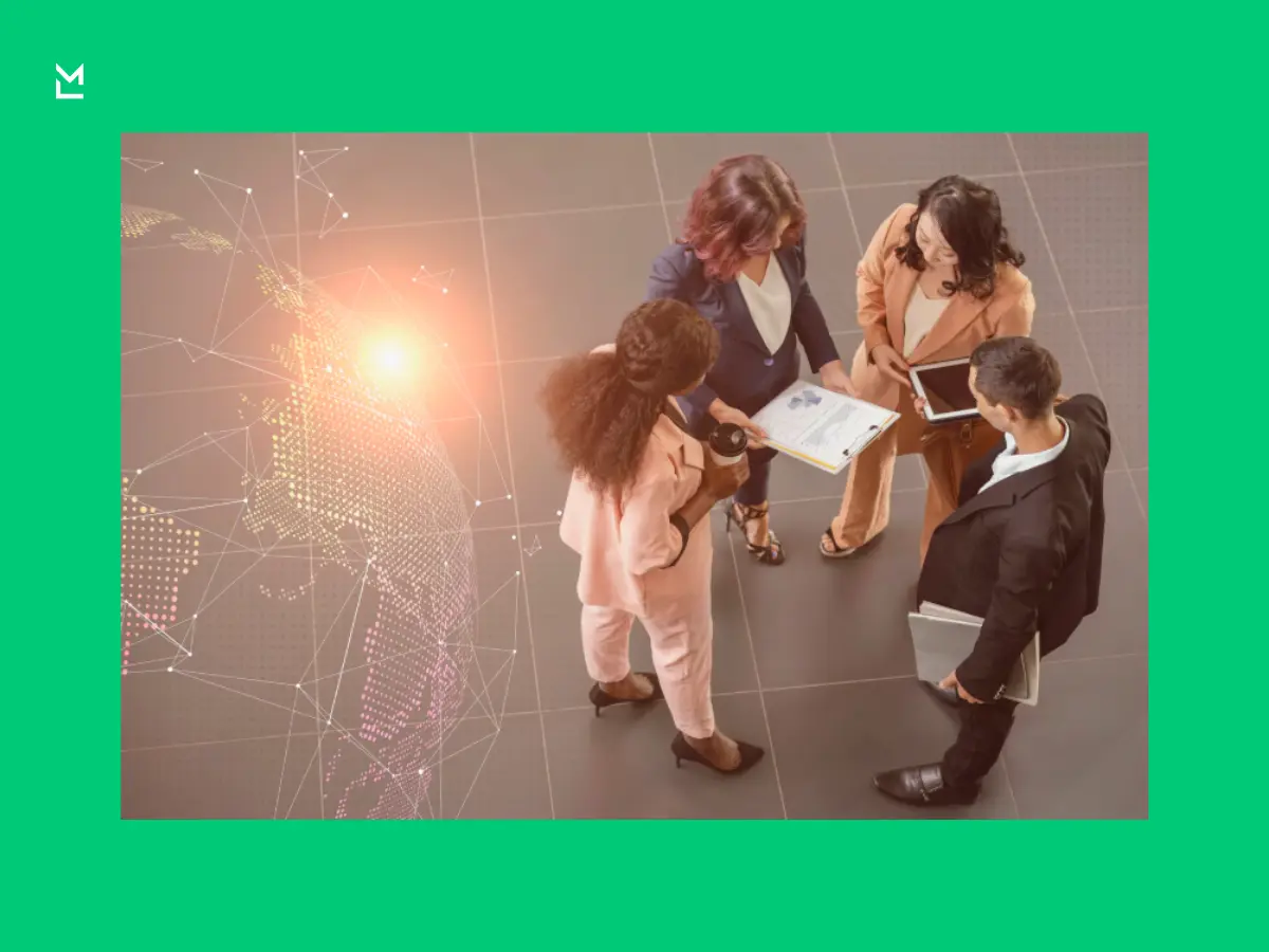 Overhead view of four business professionals standing in a circle with a tablet, clipboard, and laptop, beside a digital world map overlay signifying global connectivity.