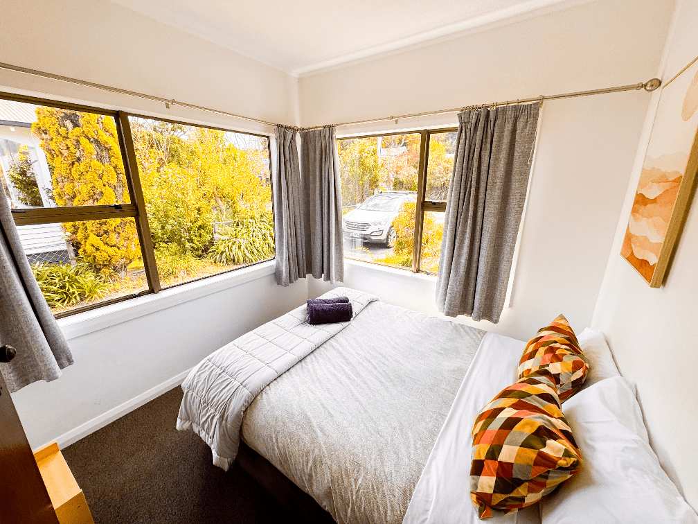 Front bedroom 1 at Russell Rumpus Retreat, a 3-bedroom plus rumpus (4-bedroom total) holiday home in Gisborne, operated by Accommodation in Gisborne—featuring large windows and a cosy queen bed.