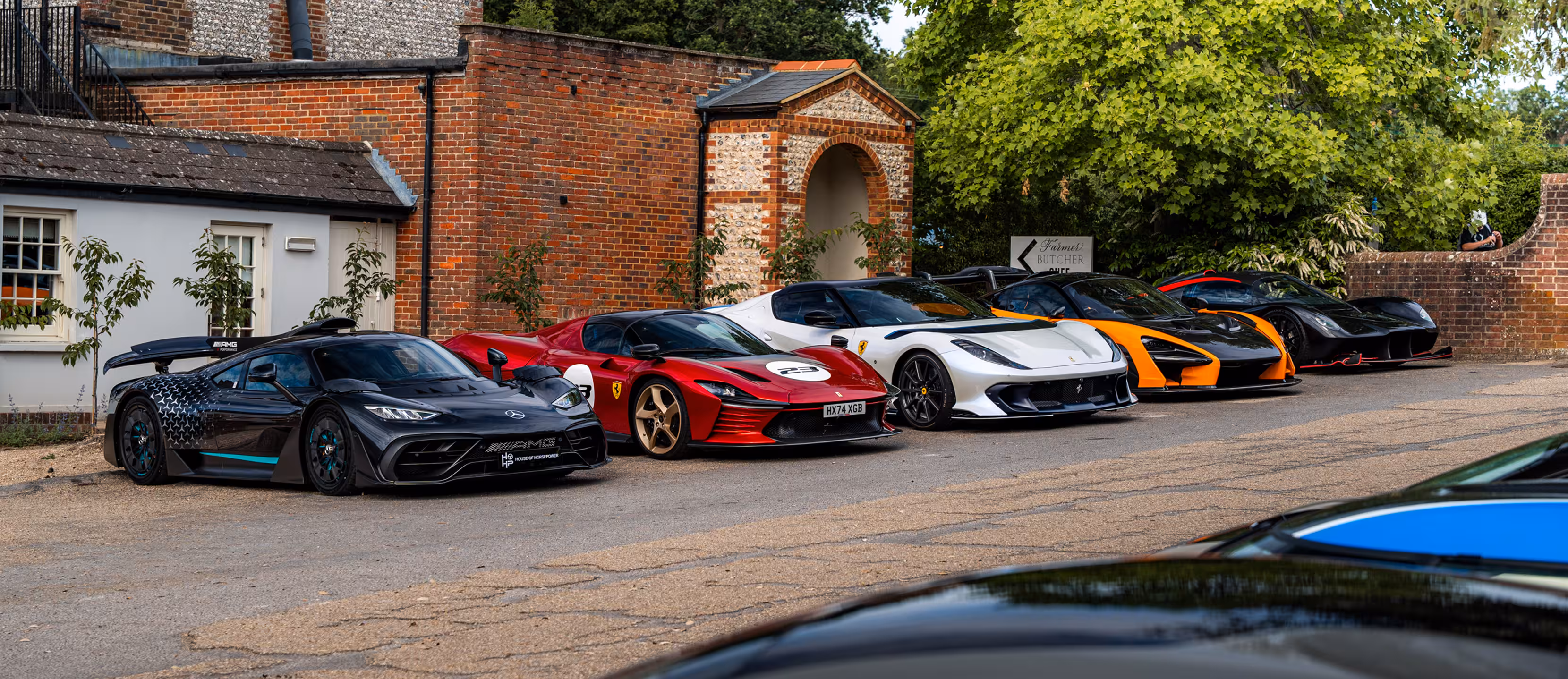Lineup of colorful luxury sports cars parked in front of a crowded grandstand with British flags and a large clock tower.