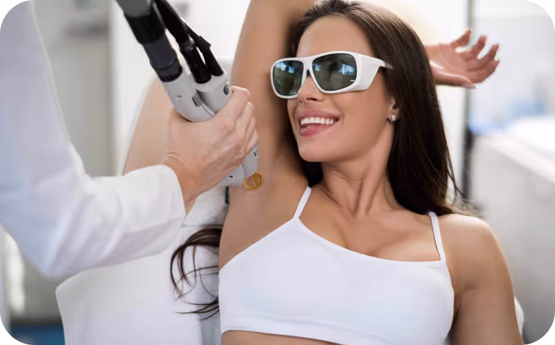 Woman wearing protective glasses smiling while receiving laser hair removal on her underarm from a professional.