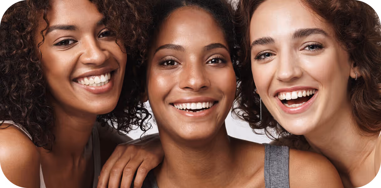 Close-up of three diverse women smiling closely together against a white background.