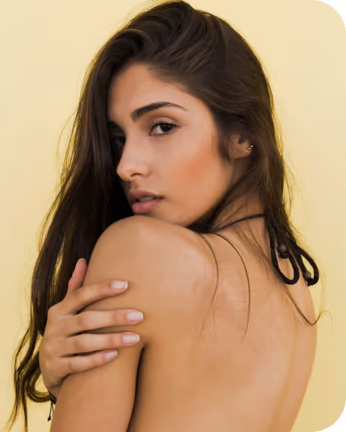 Young woman with long dark hair looking over her shoulder against a pale yellow background.