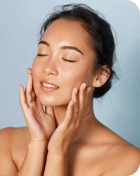 Woman with clear skin gently touching her face with closed eyes against a light blue background.