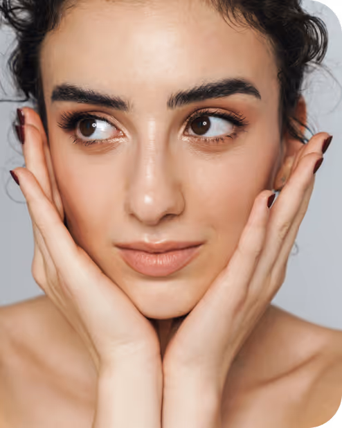 Close-up of a woman with dark curly hair, holding her face with both hands and looking sideways.