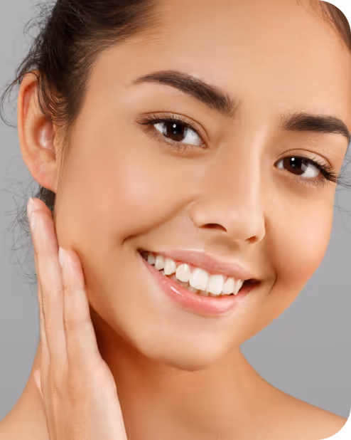 Close-up of a smiling woman with clear skin touching her cheek against a gray background.