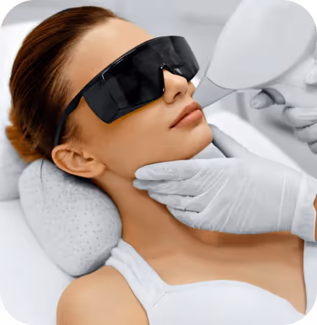 Woman wearing protective goggles receiving a laser skin treatment on her face from a gloved professional.