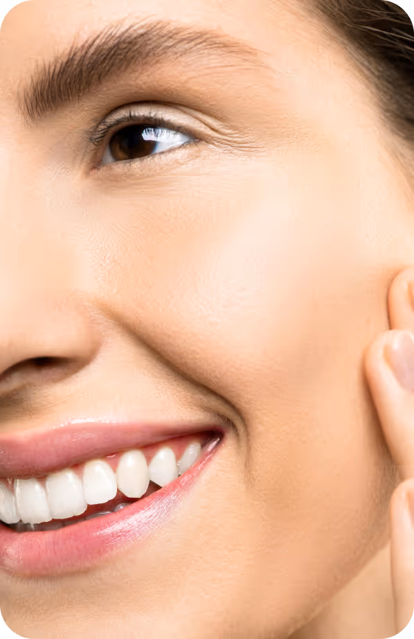 Close-up of a smiling person's face showing clear skin and white teeth, with hand gently touching the cheek.