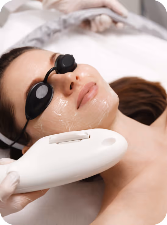 Woman wearing protective eyewear receiving a facial laser treatment with a handheld device applied to her jawline.