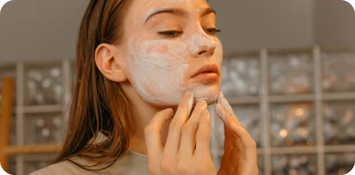 Young woman applying white facial cream to her cheek and chin with her fingers.