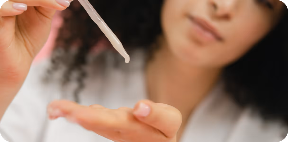 Woman holding a dropper releasing serum onto her palm, with a blurred face in the background.