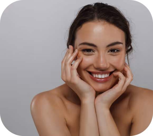 Smiling woman with bare shoulders resting her face on her hands against a gray background.