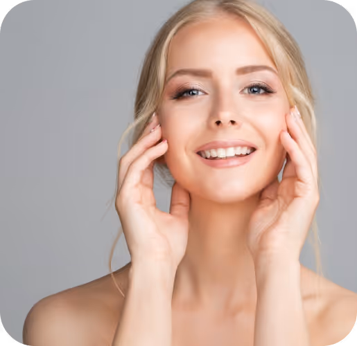 Smiling blonde woman with clear skin gently touching her face against a gray background.