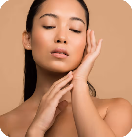 Close-up of a woman with smooth skin gently touching her face against a beige background.