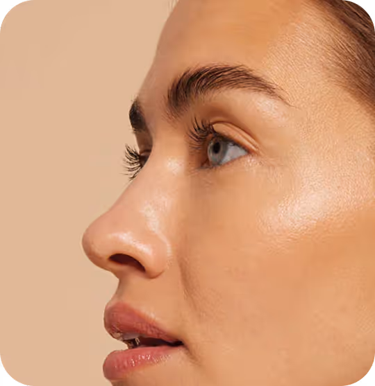 Close-up profile of a woman with smooth skin and light blue eyes against a beige background.