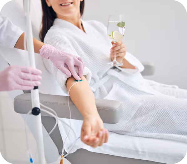 Patient in white robe holding a glass with lemon water while receiving IV treatment.