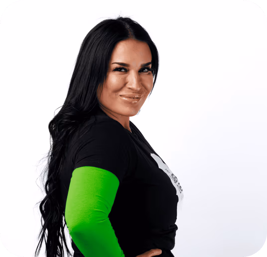 Woman with long black hair wearing a black shirt and bright green arm sleeve smiling confidently over her shoulder.