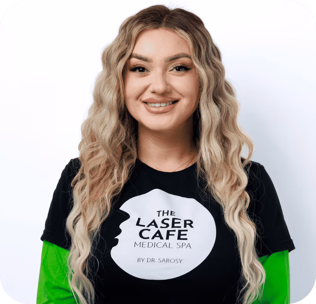 Smiling woman with long wavy blonde hair wearing a black shirt with 'The Laser Cafe Medical Spa by Dr. Sarosy' logo over a green long-sleeve top.