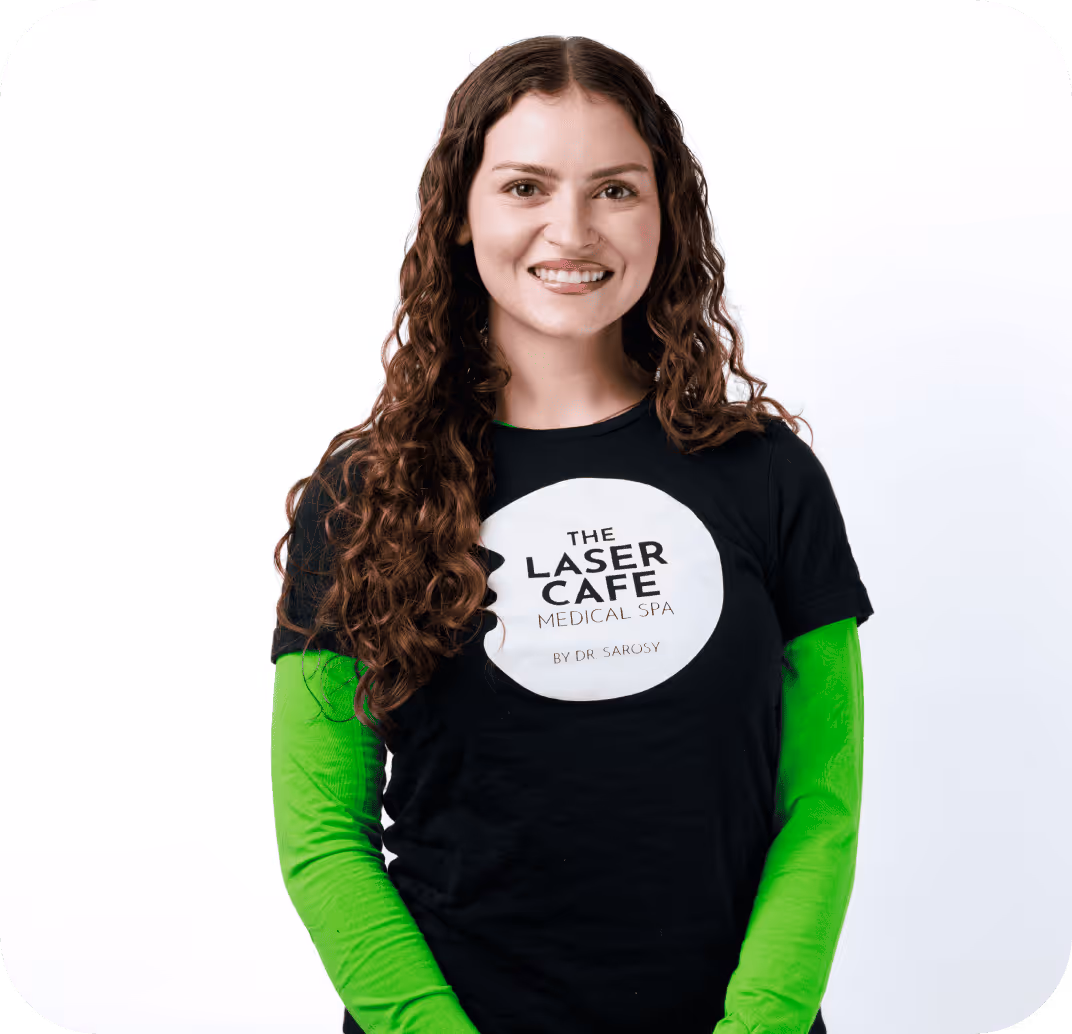 Smiling woman with long curly hair wearing a black T-shirt over a bright green long-sleeve shirt, featuring The Laser Cafe Medical Spa logo.
