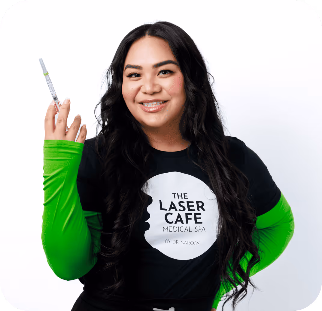 Smiling woman with long dark hair wearing a black and green shirt holding a syringe in her right hand.
