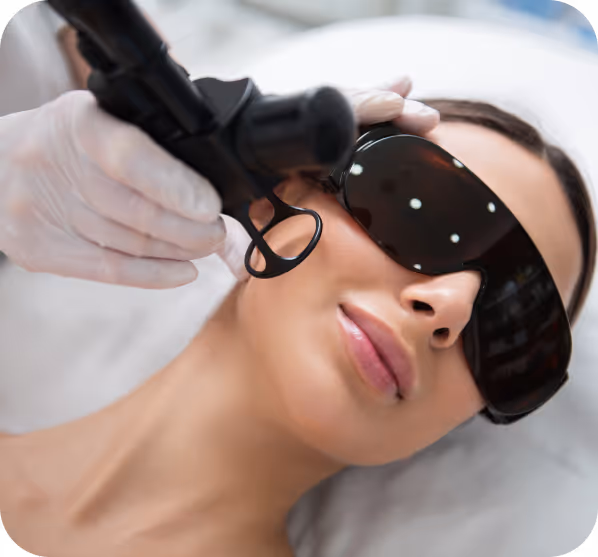 Woman wearing protective goggles receiving a laser skin treatment on her cheek from a gloved professional.