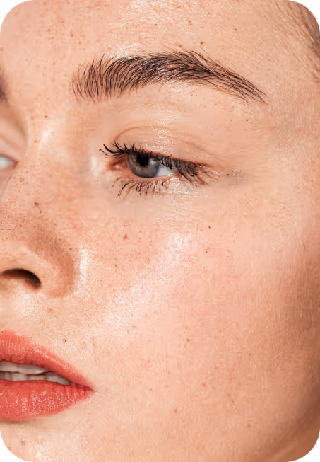 Close-up of a woman's face showing smooth, freckled skin with natural makeup and red lips.
