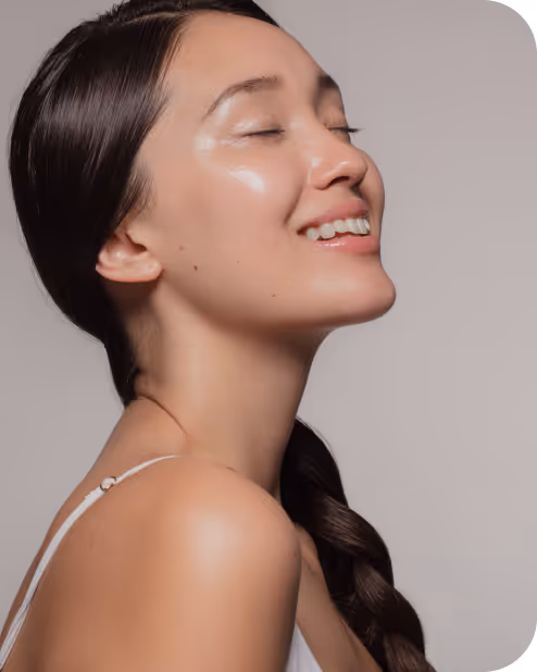 Smiling woman with closed eyes and shiny skin, wearing a white top with braided hair over her shoulder.