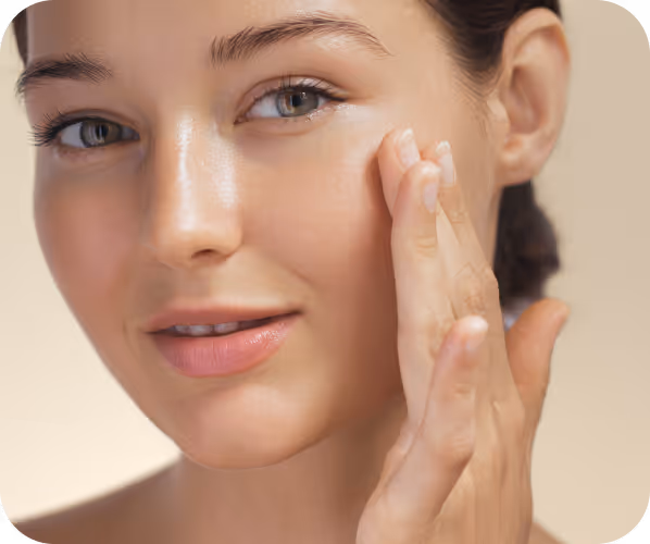 Close-up of a woman applying moisturizer to her cheek with her fingers.