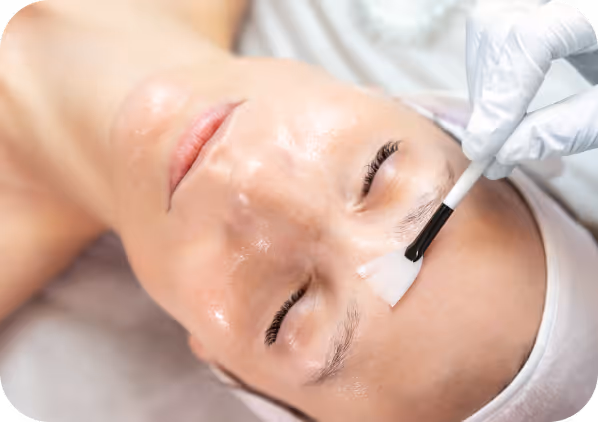 Close-up of a person receiving a facial treatment with a brush applying a skincare product to the forehead.