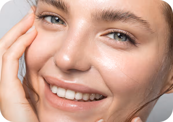 Close-up of a smiling woman with clear skin gently touching her face.