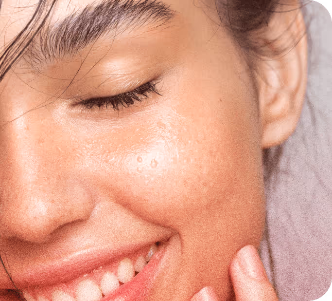 Close-up of a smiling woman with glowing, dewy skin and closed eyes.