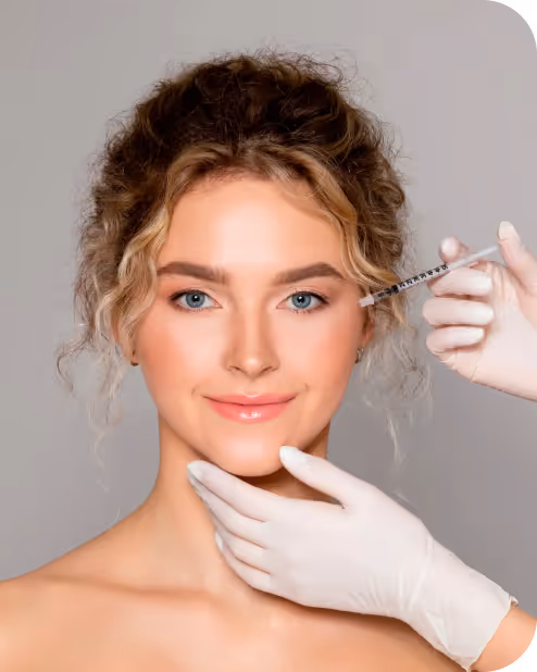 Woman with curly hair receiving a cosmetic injection near her eye from a gloved hand.